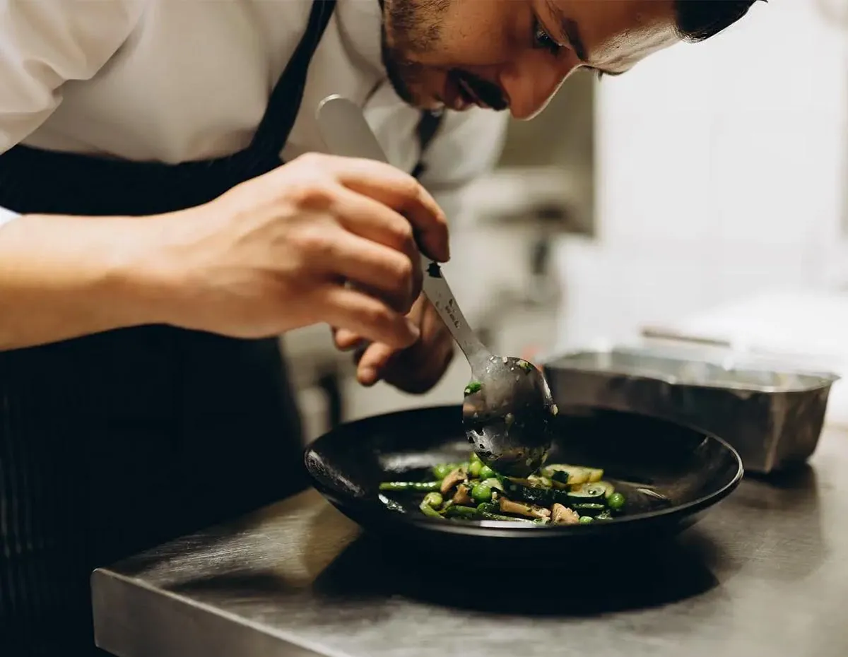 Chef cuisinier en plein dressage d'un plat de légumes de saison dans la cuisine du restaurant La Belle Quille.