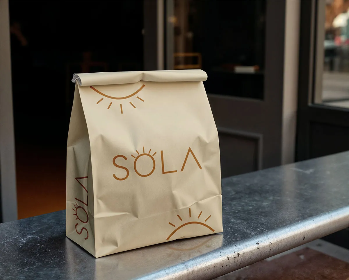Sac de transport en papier kraft avec le logo SOLA et des motifs de soleil pour la vente à emporter.