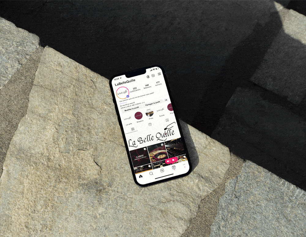 Animation montrant le profil Instagram du restaurant La Belle Quille sur un écran de smartphone posé sur de la pierre.