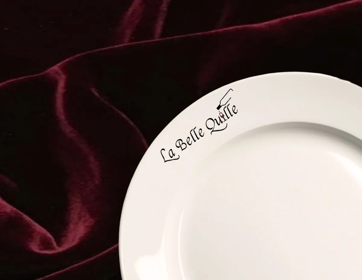 Logo noir du restaurant La Belle Quille imprimé sur le rebord d'une assiette blanche sur fond velours bordeaux.